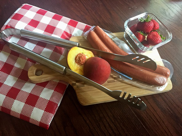 Grill Tongs with sausage and fruit on cutting board